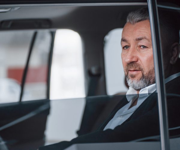 Break between trip. Senior businessman in official clothes sitting in a modern new car.