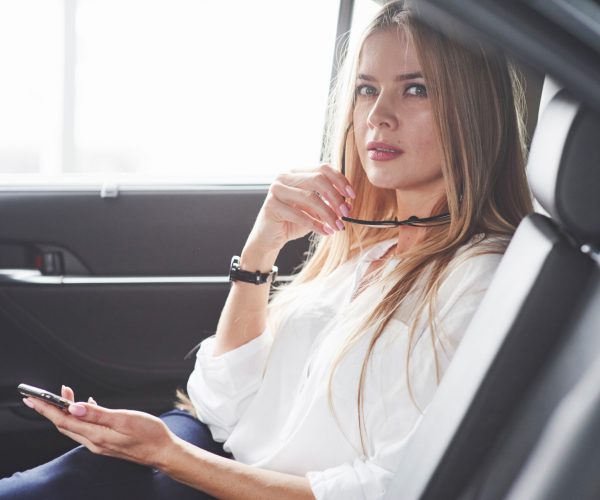 Natural lighting. Beautiful blonde girl sitting in the new car with modern black interior.