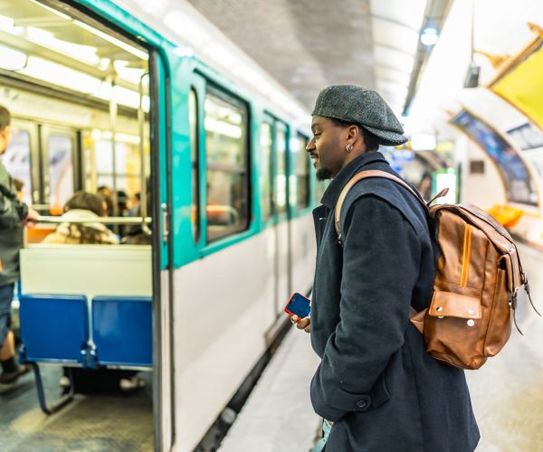 Young man stands on a bustling paris metro platform, looking toward an open train door as passengers board and depart during a busy daily commute